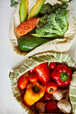 Üst manzara, yeniden kullanılabilir pamuklu poşetlerdeki taze sebzeler, gün ışığında Kitche 'deki masada, tekstil sıfır atık torbalarındaki bakkallar, internette sağlıklı alışveriş, vejetaryen yiyecekler..