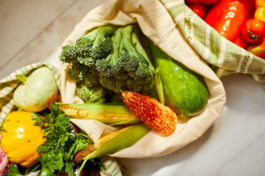 Üst manzara, yeniden kullanılabilir pamuklu poşetlerdeki taze sebzeler, gün ışığında Kitche 'deki masada, tekstil sıfır atık torbalarındaki bakkallar, internette sağlıklı alışveriş, vejetaryen yiyecekler..