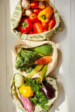 Üst manzara, yeniden kullanılabilir pamuklu poşetlerdeki taze sebzeler, gün ışığında Kitche 'deki masada, tekstil sıfır atık torbalarındaki bakkallar, internette sağlıklı alışveriş, vejetaryen yiyecekler..