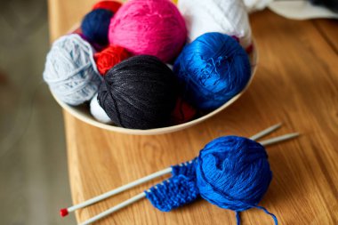 Ahşap masada çok renkli örgü ipliği, sepetteki iplik yumakları örgü iğneleri, kopyalama alanı..