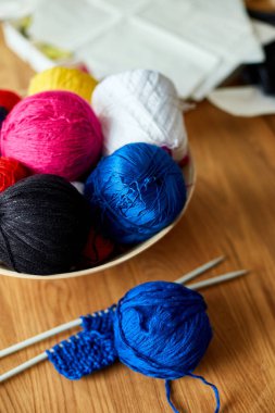 Ahşap masada çok renkli örgü ipliği, sepetteki iplik yumakları örgü iğneleri, kopyalama alanı..