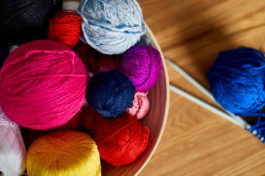 Ahşap masada çok renkli örgü ipliği, sepetteki iplik yumakları örgü iğneleri, kopyalama alanı..