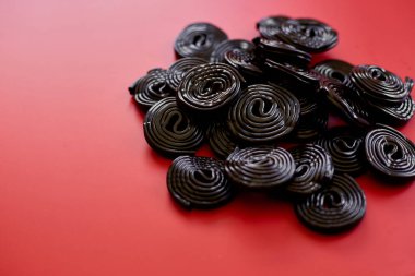 Kırmızı arka planda siyah meyan kökü şekeri, şeker aromalı meyan kökü, üst manzara..