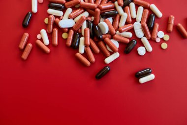 Kırmızı arka planda farklı renkte tıbbi haplar, vitamin eksikliği, avitaminoz konsepti, çeşitli ilaç hapları, beslenme destek ürünleri.