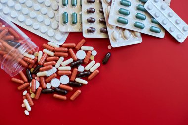 Kırmızı arka planda farklı renkte tıbbi haplar, vitamin eksikliği, avitaminoz konsepti, çeşitli ilaç hapları, beslenme destek ürünleri.