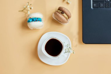 Düz uzanış, üst düzey ofis masası, dizüstü bilgisayarlı çalışma alanı, kahve fincanı ve çiçekli badem kurabiyesi, turuncu arka planda, evden çalışma, uzak çalışma