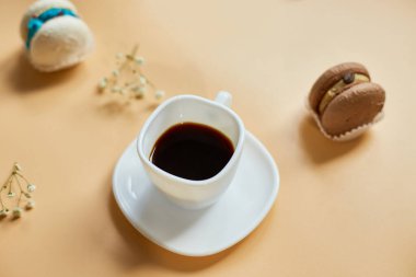 Üst manzara, düz pasta makaronu, Fransız kurabiyeleri, turuncu arka planda bir fincan kahve, renkli badem kurabiyeleri, pastel renkler, yaratıcı ve moda kompozitosu.