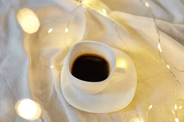 Cup of coffee in bed with a gerlands lights, copy space. Greeting card, romantic breakfast, christmas concept.