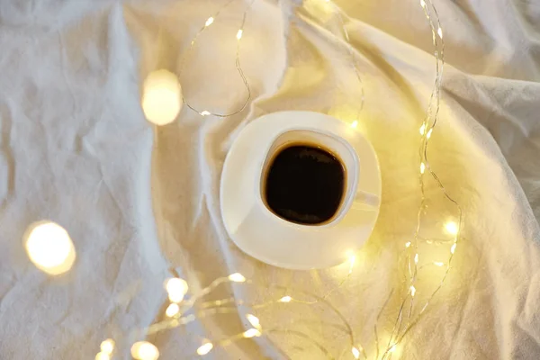 Cup of coffee in bed with a gerlands lights, copy space. Greeting card, romantic breakfast, christmas concept.