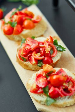 İtalyan bruschetta 'sı taze kırmızı domatesler ve fesleğenli otlar bahçedeki ahşap tahta üzerinde, arka bahçede, evde, gün ışığında. Klasik İtalyan yemeği, antipasto.