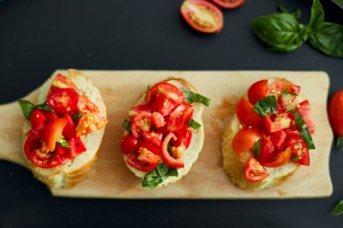 İtalyan bruschetta 'sı taze kırmızı domatesler ve fesleğenli otlar bahçedeki ahşap tahta üzerinde, arka bahçede, evde, gün ışığında. Klasik İtalyan yemeği, antipasto.