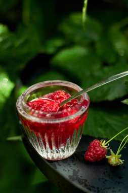 Siyah arka planda cam kasede ahududu reçeli, açık hava bahçesi taze çalı, güneş ışığı. 