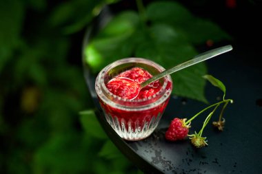 Siyah arka planda cam kasede ahududu reçeli, açık hava bahçesi taze çalı, güneş ışığı. 