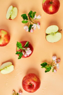 Dilimlenmiş, bütün kırmızı elma ve çiçekler pastel turuncu arka planda bir düz, meyveler ve çiçekler, sping konsepti. Üst görünüm
