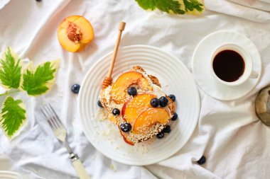 Top view Breakfast on white bed sheets, good morning, summer french toast with cream cheese, honey, peaches and blueberries, coffee, flowers, Hotel room early morning, honeymoon