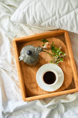 Coffee cup, geyser coffee maker and flowers on tray on white bed sheets, good morning,  Hotel room early morning, breakfast in the bed