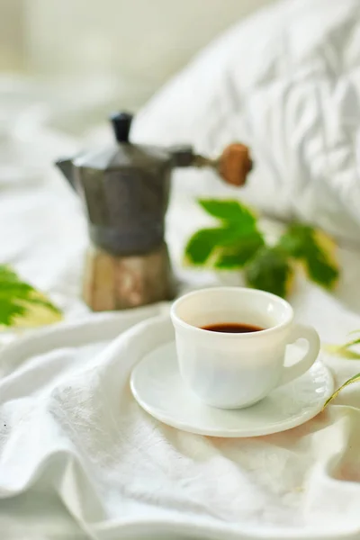 Coffee cup on white bed sheets with geyser coffee maker and  green leaves, good morning,  Hotel room early morning, breakfast in the bed