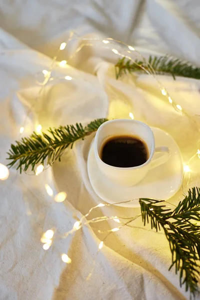 Cup of coffee in bed with a gerlands, needles and lights, copy space. Greeting card, romantic breakfast, christmas concept.