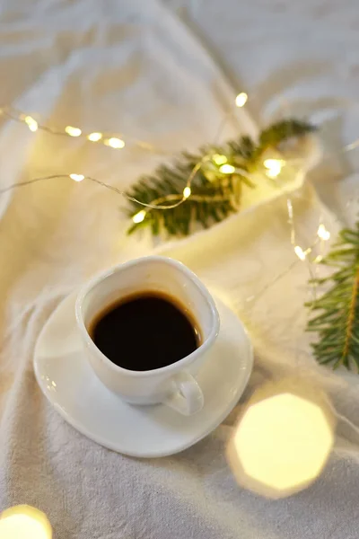 Cup of coffee in bed with a gerlands, needles and lights, copy space. Greeting card, romantic breakfast, christmas concept.