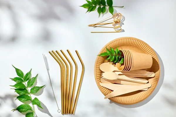 Set of eco friendly tableware, reusable disposable plates, cups, stainless steel straws and cleaning brush on white background with hard light shadow. Biodegradable craft dishes, recycling concept