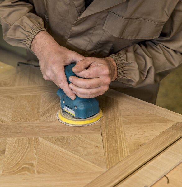 close up of carpenter's hand using a grinder on a wood surface