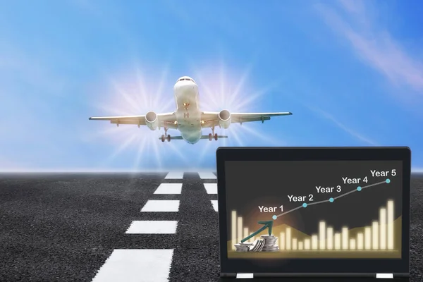 Commercial plane ready for landing or taking off with growth graph on computer notebook on runway background. Airplane business recovery concept and return on investment idea