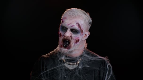 Зловещий человек в костюме чокнутого зомби Хэллоуина с окровавленными шрамами на лице пытается напугать — стоковое видео