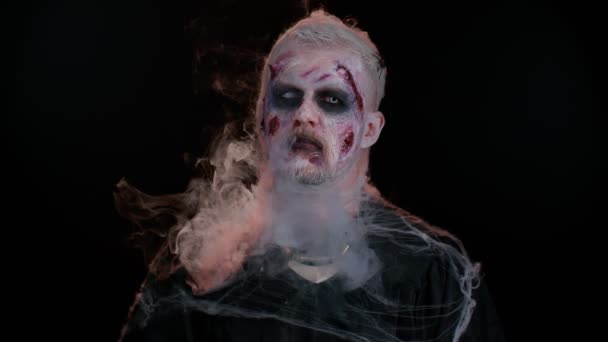 Ijesztő ember Halloween zombi smink fúj füst az orr és a száj, megpróbálja megijeszteni — Stock videók