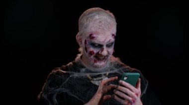 Korkunç adam Cadılar Bayramı zombisi cep telefonu kullanıyor internette yeni bir yazı yazıyor, internette geziniyor, bağımlılık yapıyor.