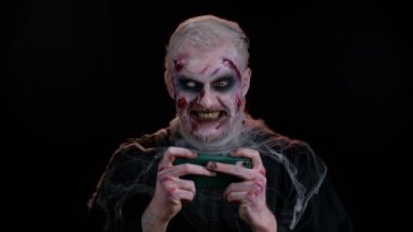 Uğursuz adam Cadılar Bayramı zombisi cep telefonunda yarış sürüşü video oyunları oynuyor
