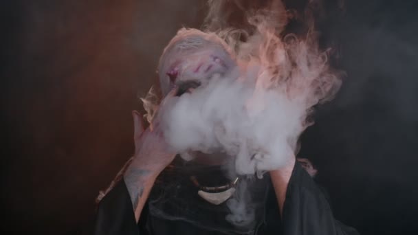 Ijesztő ember Halloween zombi véres sebesült bujkál a kéz mögött fúj füst az orr és a száj — Stock videók