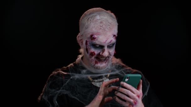 Ijesztő ember Halloween zombi segítségével mobiltelefon gépelés új hozzászólás a weben, böngészés, függőség — Stock videók