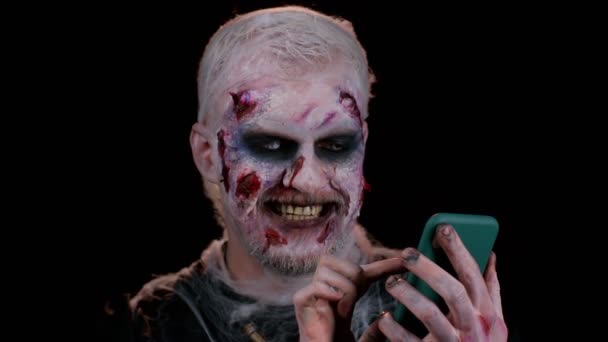 Ijesztő ember Halloween zombi segítségével mobiltelefon gépelés új hozzászólás a weben, böngészés, függőség — Stock videók