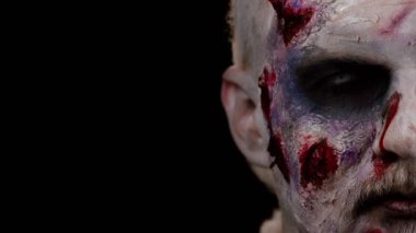 Zombi adam makyajla yüzleşiyor. Yara izleri ve beyaz lenslerle kameraya bakıp onu korkutmaya çalışıyor.