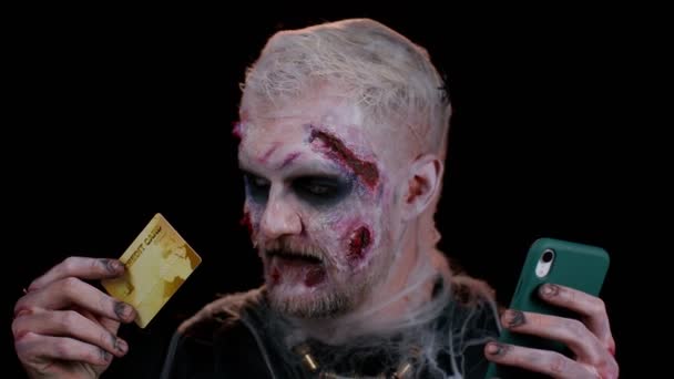 Hombre siniestro Halloween zombie usando tarjeta bancaria de crédito y teléfono inteligente mientras compra compras en línea — Vídeos de Stock