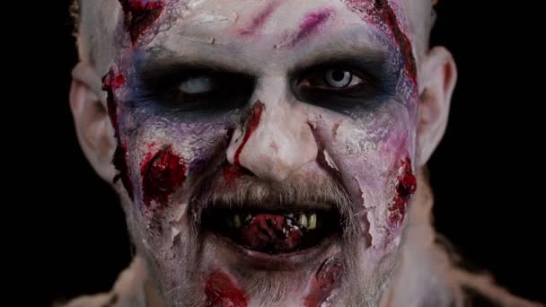 Zombie hombre con cicatrices heridas y lentes de contacto mirando la cámara hace clic en sus dientes tratando de asustar — Vídeos de Stock