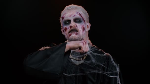Sinister man Halloween zombie trying to scare showing killing gesture, runs a finger along his neck — Stock Video