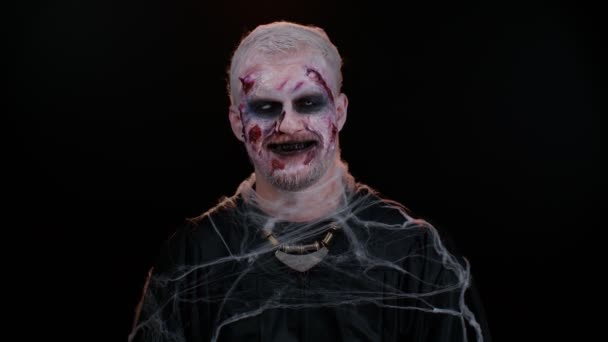 Веселый жуткий человек Хэллоуин зомби корчит рожи, смотрит в камеру, ужасно улыбается грязными зубами — стоковое видео