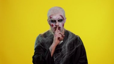 Cadılar Bayramı zombisi, işaret parmağını dudaklarına bastırıyor. Sessiz jest işareti yapıyor.