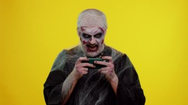 Uğursuz adam Cadılar Bayramı zombisi cep telefonunda yarış sürüşü video oyunları oynuyor