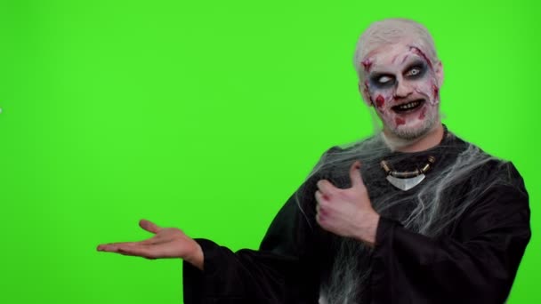 Asustadizo herido Halloween zombie no muerto hombre mostrando pulgares hacia arriba y señalando a la izquierda en el espacio en blanco — Vídeos de Stock