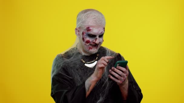 Hombre aterrador Halloween zombie usando el teléfono móvil escribiendo nuevo post en la web, navegación, adicción — Vídeos de Stock