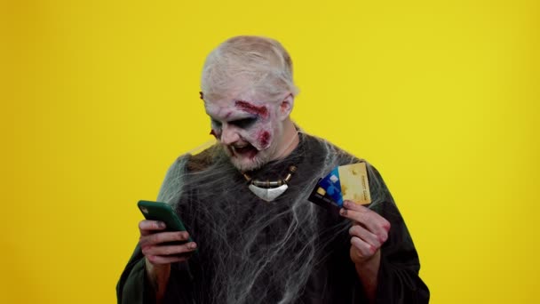 Homem sinistro Halloween zumbi usando cartões bancários de crédito e smartphone enquanto compra compras on-line — Vídeo de Stock