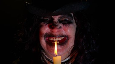 Cadılar Bayramı cadısının karnaval kostümlü uğursuz yaşlı kadın mumla sihirli ayinler yapıyor.