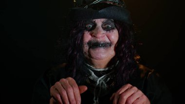 Cadılar Bayramı cadı makyajlı ürkütücü yaşlı nine kameraya bakıyor, korkutmaya çalışıyor, yüz ifadeleri takınıyor