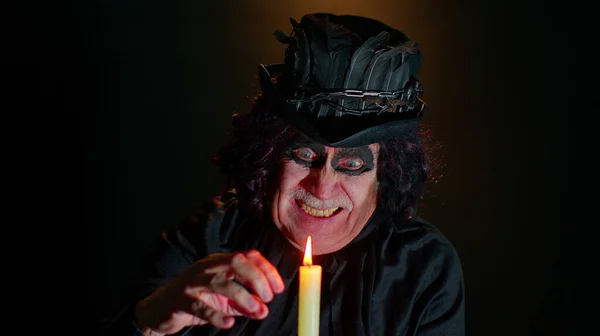 Homem sênior sinistro em traje de carnaval de bruxo Halloween sopra fumaça da boca, tentando assustar — Fotografia de Stock