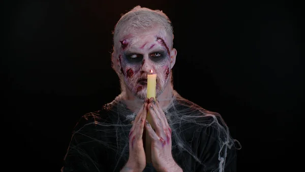 Aterrador hombre con Halloween zombie sangrientos hechizos de maquillaje evoca sobre velas, rituales vudú —  Fotos de Stock