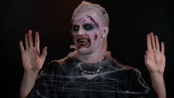 Zombie Halloween hombre con cicatrices heridas cara usando auriculares, escuchando música, bailando, celebrando —  Fotos de Stock