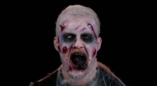 Frightening scary man with Halloween zombie bloody wounded makeup, showing tongue, trying to scare