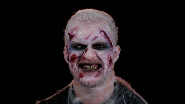 Sinister man in costume of Halloween crazy zombie with bloody wounded scars face trying to scare